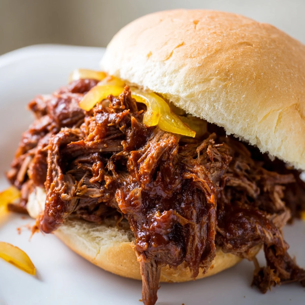 Fork-tender shredded beef from Slow Cooker Pulled Beef Sandwiches served on a toasted bun with crisp pickles.