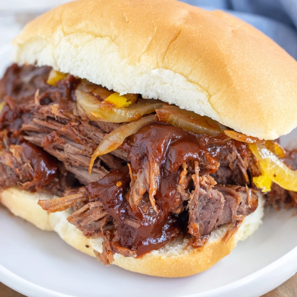 Golden buns holding Slow Cooker Pulled Beef Sandwiches, garnished with red onion and fresh coleslaw for a weeknight meal.