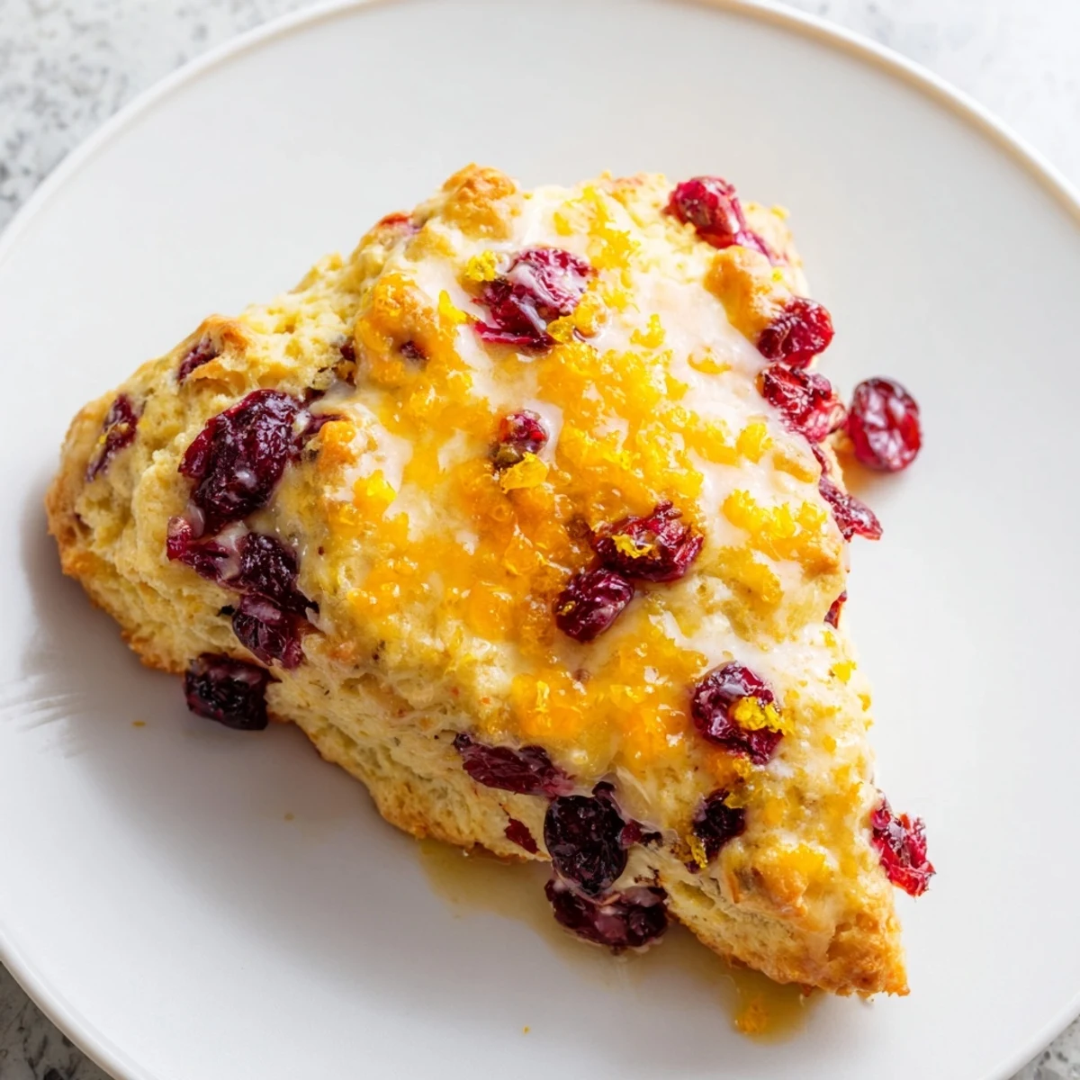 Warm Cranberry Orange Scones with Orange Glaze drizzled with icing, perfect for a cozy breakfast plate.
