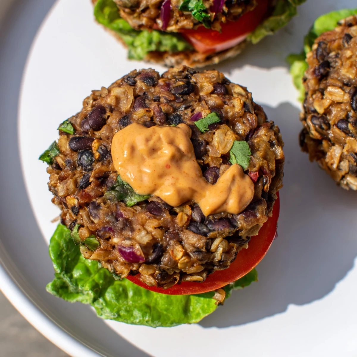 Close-up of smoky vegan black bean burger topped with creamy spicy chipotle mayo and fresh avocado slices.