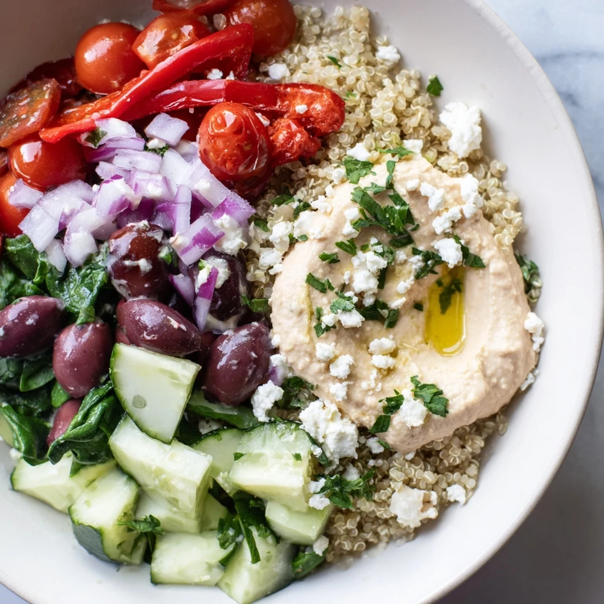 Mediterranean Quinoa Bowl topped with creamy hummus, vibrant cherry tomatoes, cucumber, and a drizzle of zesty lemon-tahini dressing.