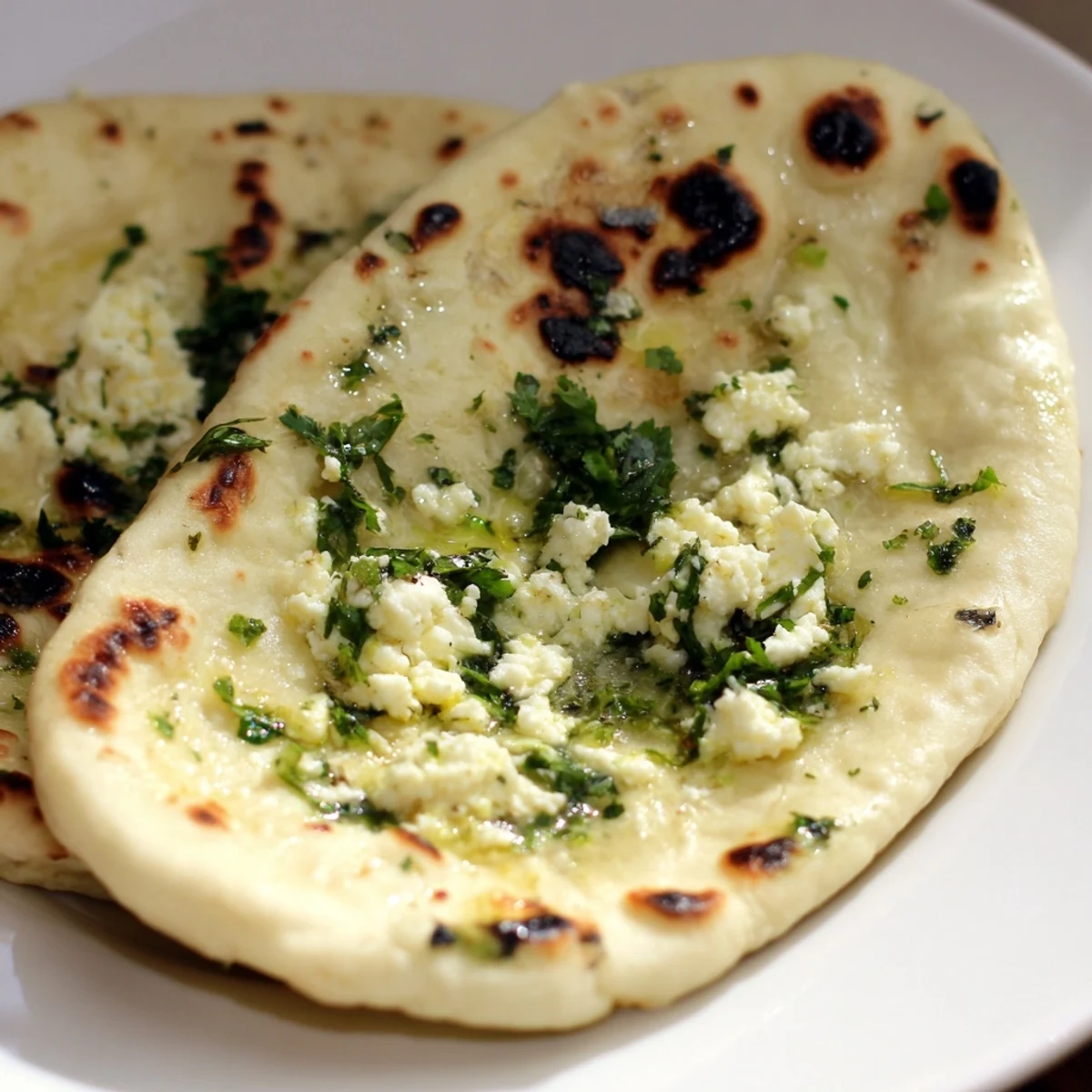 A warm Cottage Cheese Garlic Naan brushed with butter and herbs sits beside a bowl of curry for a hearty meal.