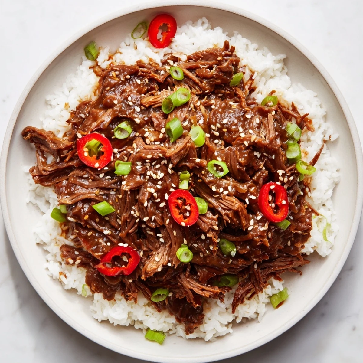 A close-up of Slow Cooker Korean Beef shredded and glistening with savory-sweet sauce, garnished with green onions and sesame seeds.
