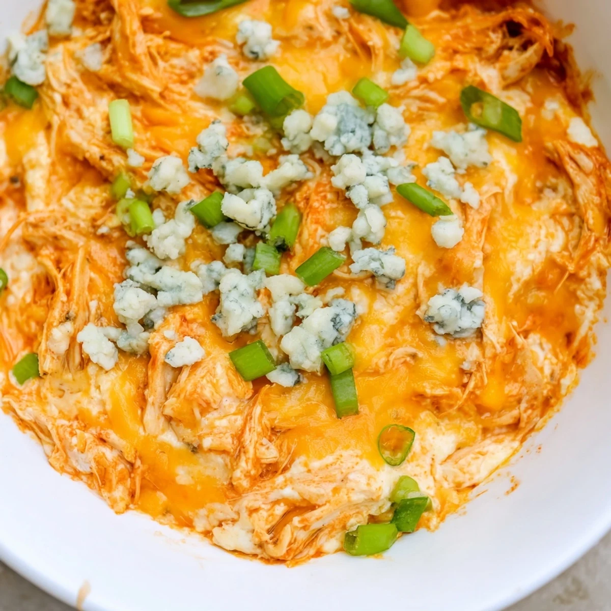Golden, bubbly Keto Buffalo Chicken Dip in a baking dish, garnished with fresh green onions and served with crisp celery sticks for dipping.