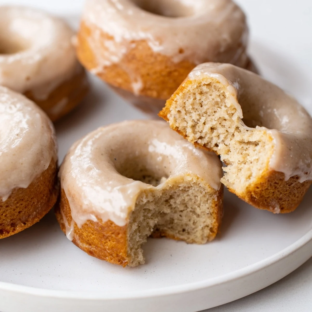 Warm Baked Banana Bread Donuts showing moist interior, with optional glaze drizzle and specks of cinnamon throughout.