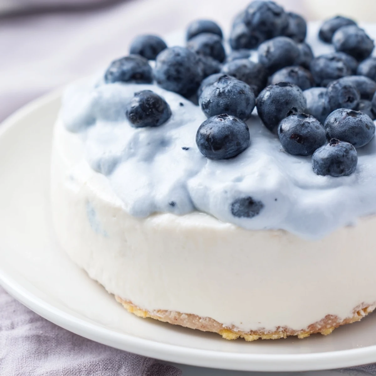 A slice of Blueberry Mousse Cheesecake on a plate with a fork, featuring a creamy filling and fresh blueberries for a summer dessert.