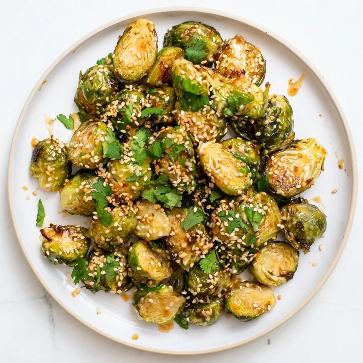 A close-up of crispy roasted Honey Sriracha Brussels Sprouts drizzled with the sweet and spicy glaze, served alongside grilled chicken for dinner.