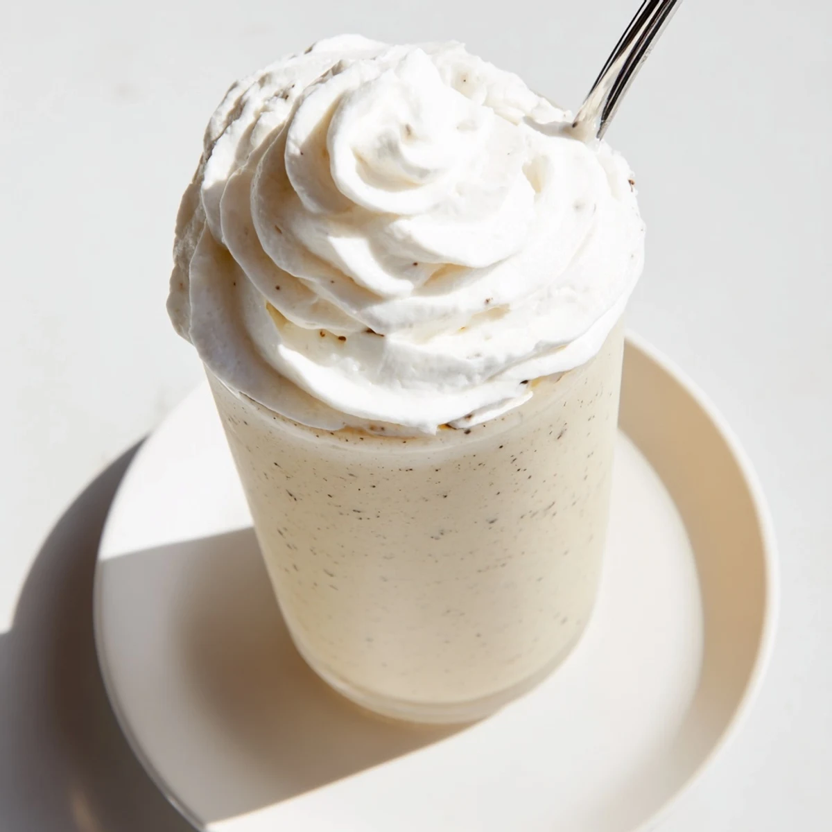 Homemade Vanilla Bean Frappuccino poured over ice cubes beside fresh vanilla beans for a refreshing coffeehouse-style treat.