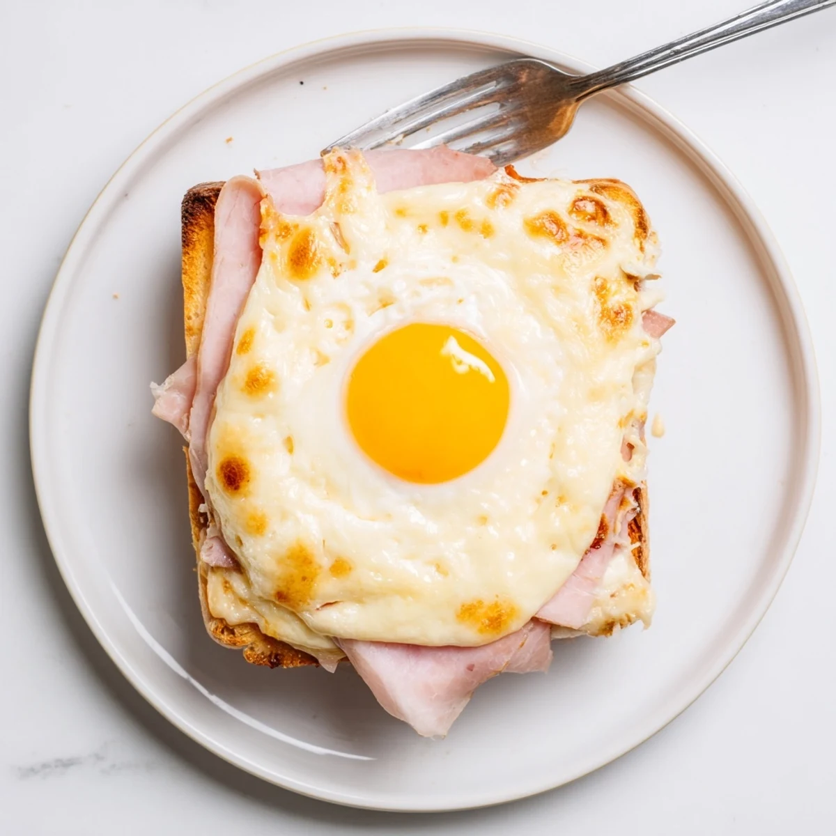 The classic Croque Madame breakfast sandwich, featuring crispy toast, creamy béchamel sauce, and a perfectly runny egg yolk.