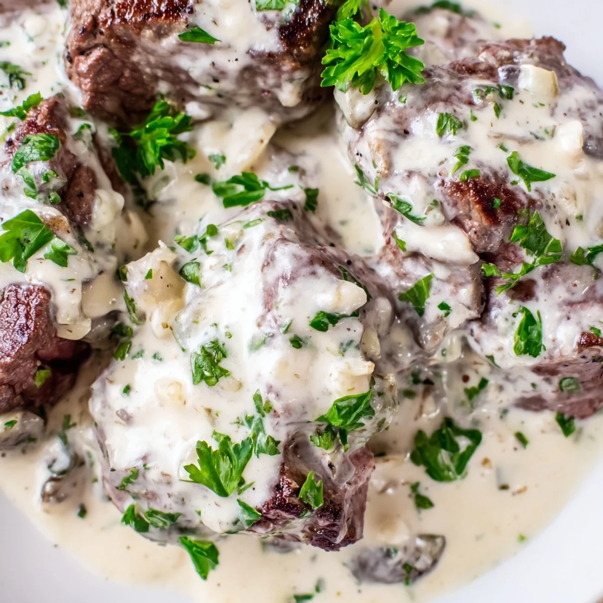 Seared Garlic Butter Steak With Parmesan Cream Sauce rests on a plate, garnished with fresh parsley.