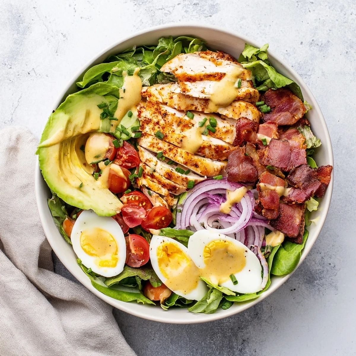 Freshly grilled chicken slices glisten over mixed greens with avocado, bacon, and cherry tomatoes in this Paleo Grilled Chicken Cobb Salad With Honey Dijon Dressing.