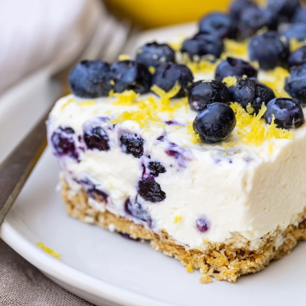 Creamy no bake lemon blueberry cake slice with graham cracker base and scattered fresh berries