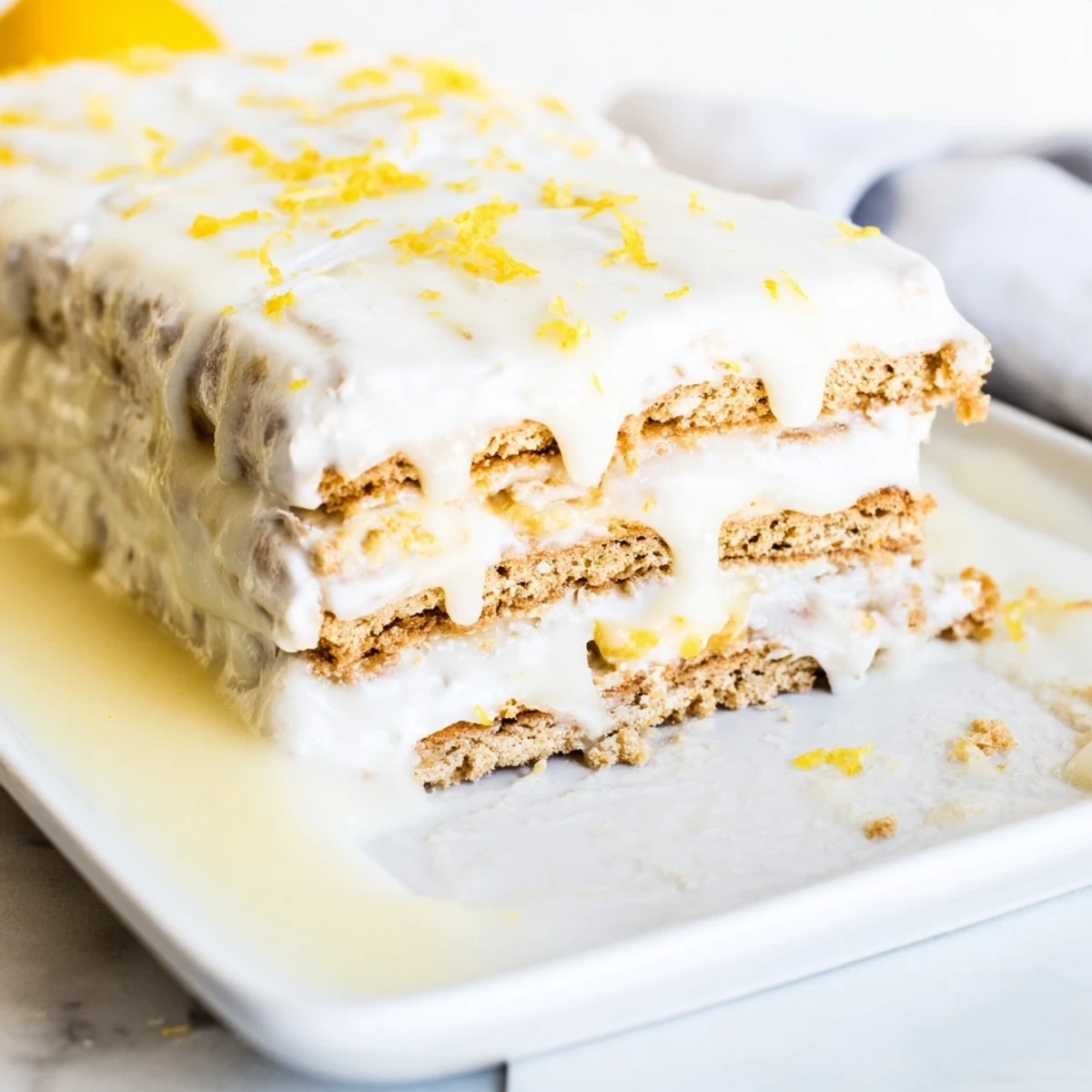 No bake lemon eclair cake sliced into squares on a white serving plate, showcasing creamy lemon layers between softened graham crackers and topped with glossy lemon glaze