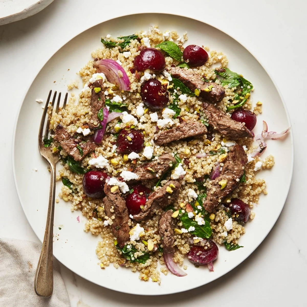 Colorful cherry quinoa salad with lamb topped with crumbled feta and fresh herbs