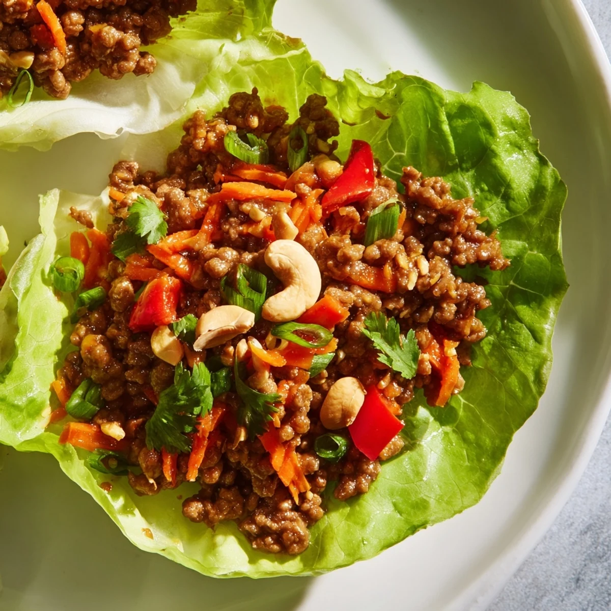 Garnished beef and cashew lettuce cups showcase colorful diced vegetables, herbs, and lime wedges for serving