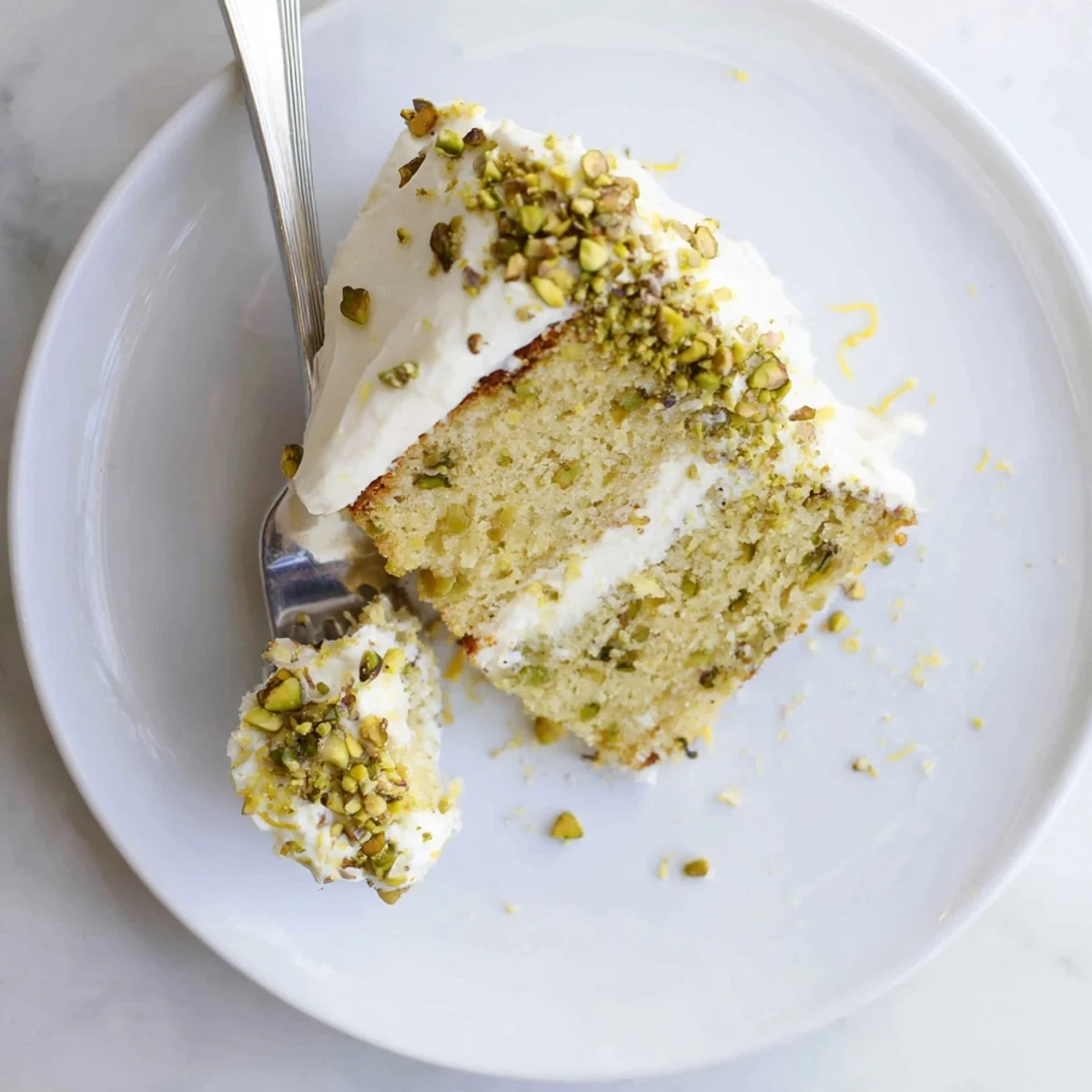 Moist lemon pistachio cake with smooth mascarpone cream frosting sprinkled with fresh nuts and lemon zest