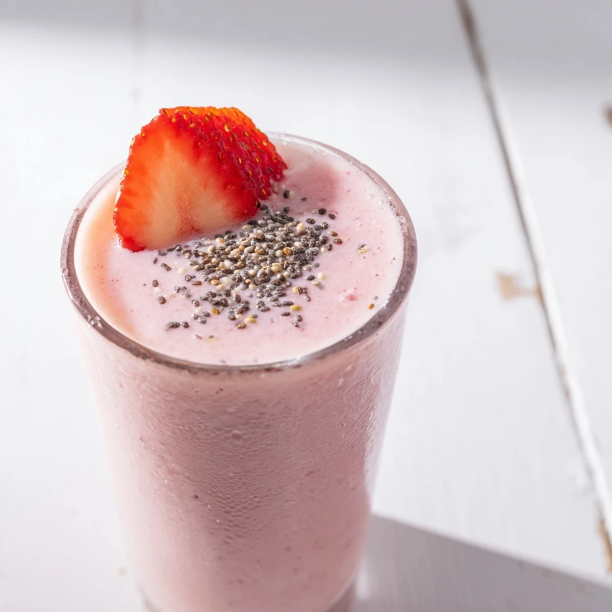 Vibrant strawberry yogurt smoothie garnished with whole strawberry on white background