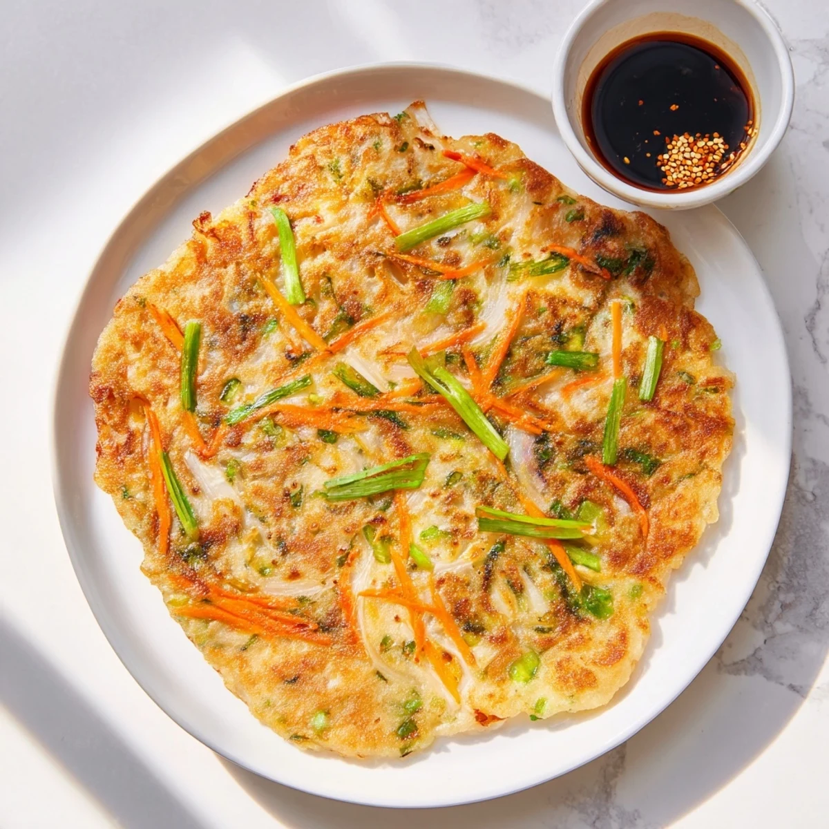 Golden crispy Korean pancakes loaded with fresh scallions and colorful julienned vegetables on a white plate