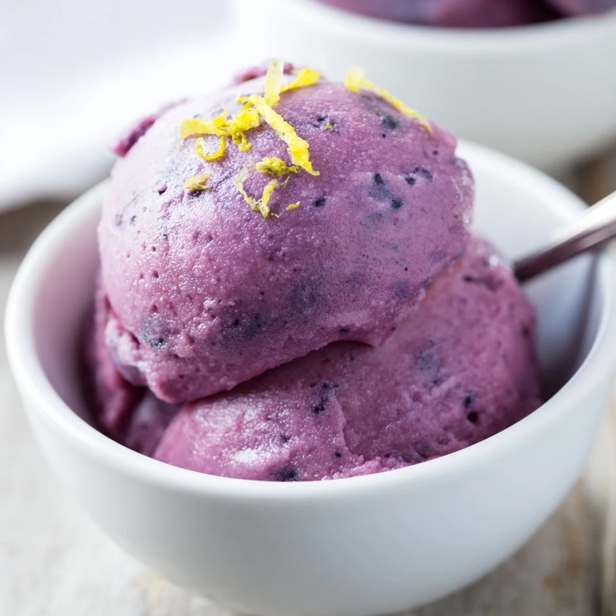 Purple swirls of homemade no churn blueberry lemon sorbet melting in glass dessert bowls
