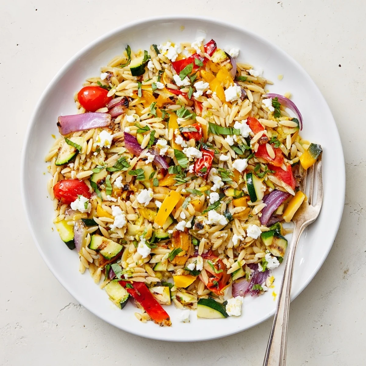 Hearty vegetable orzo dish featuring peppers zucchini and cherry tomatoes with basil sprinkles on top