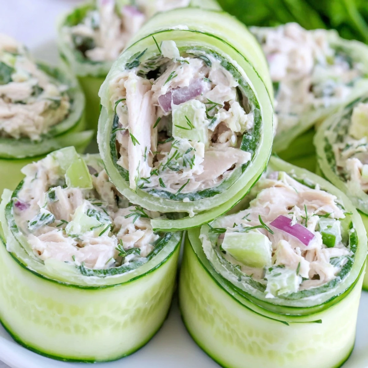 Fresh cucumber ribbons wrapped around creamy chicken salad mixture on a white serving platter