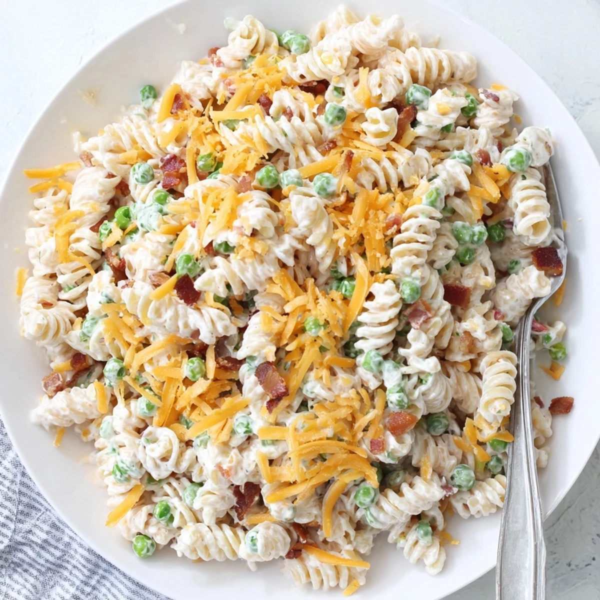 Cold pasta salad featuring rotini noodles, sharp cheddar, green onions, and golden bacon garnish