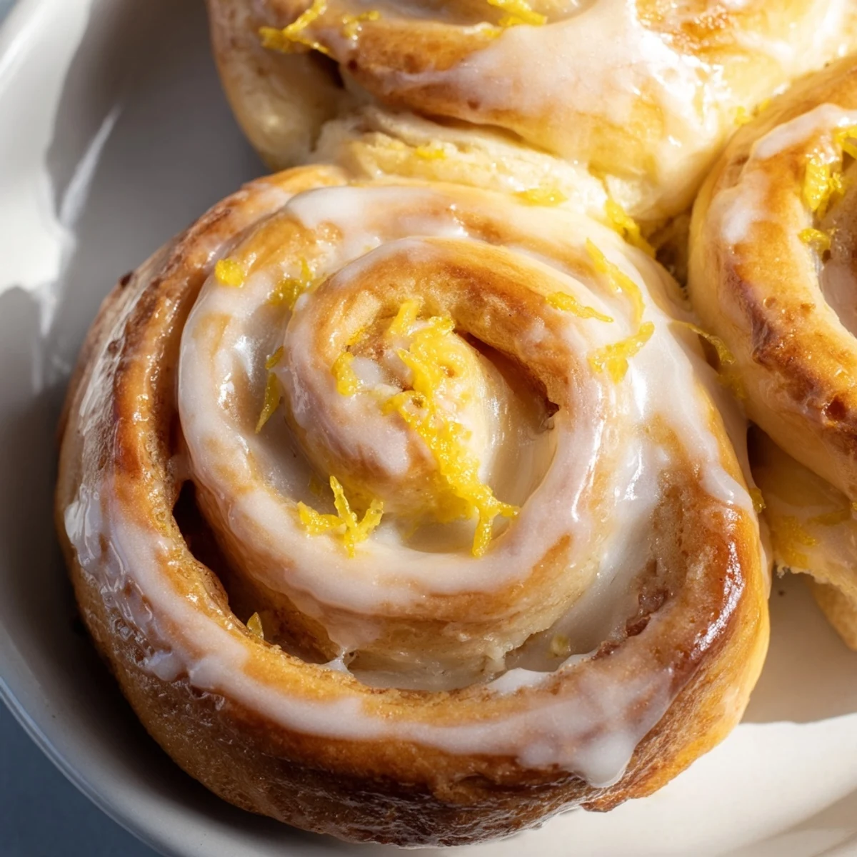 Golden lemon rolls drizzled with tangy glaze on a white serving plate