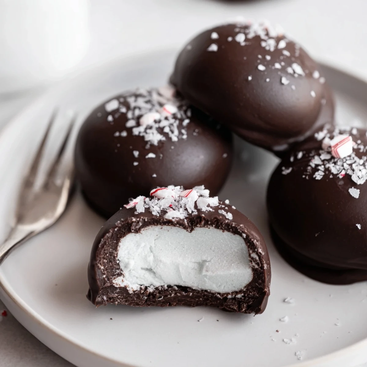 Glossy dark-chocolate Peppermint Patties resting on parchment, flecks of crushed peppermint.