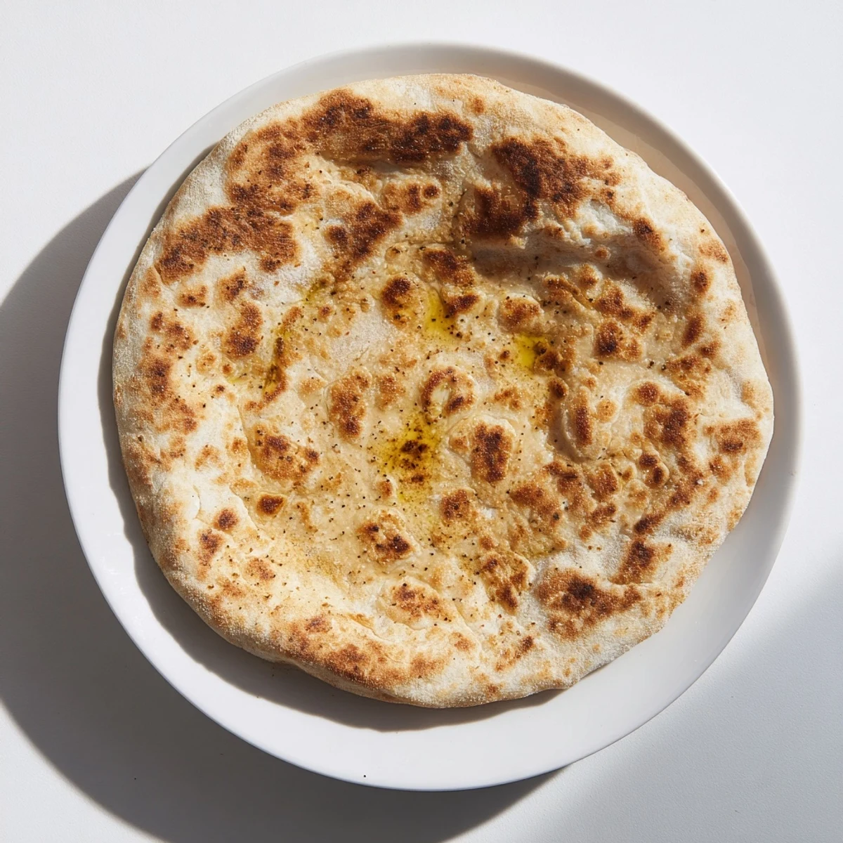 Warm Turkish Bazlama flatbread stacked high with brush of olive oil on soft surface