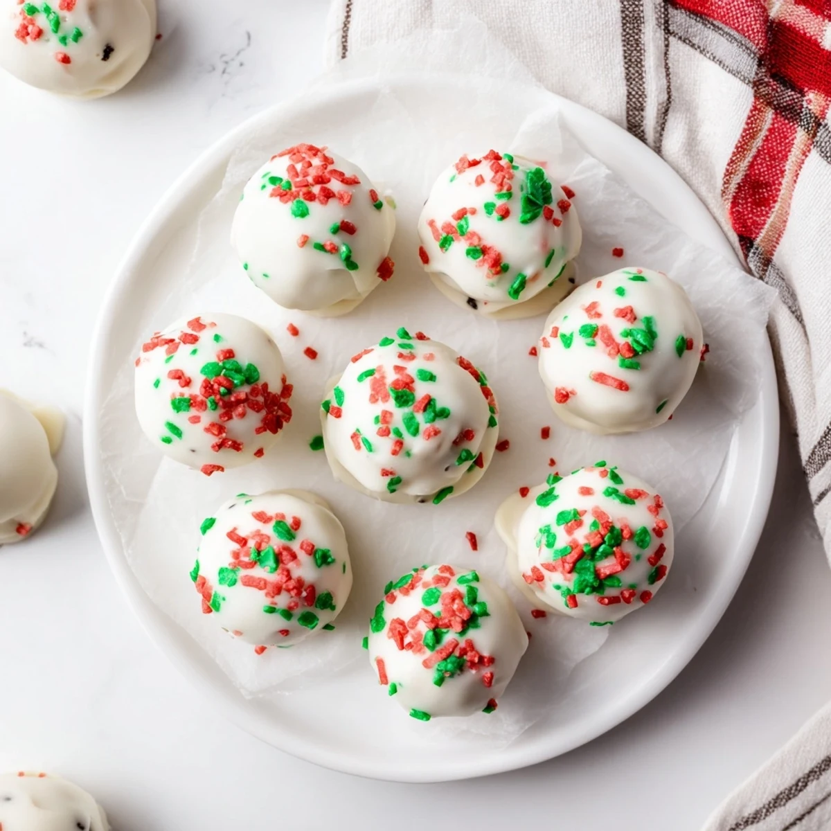 Golden Oreo truffles coated in smooth white chocolate topped with red and green sprinkles on a white plate