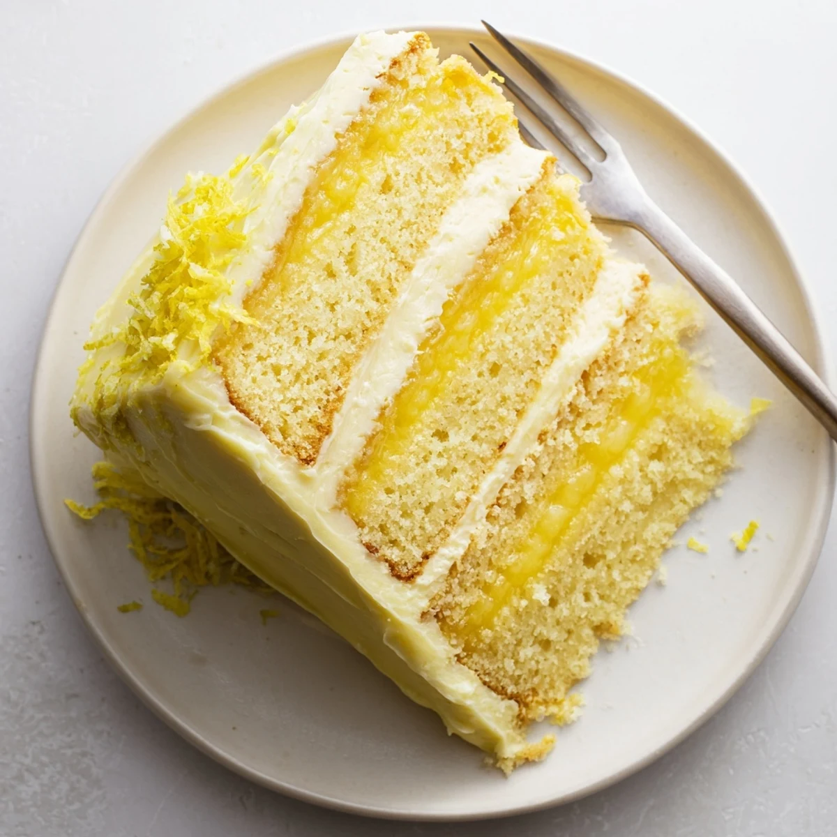 Triple-layer lemon layer cake sliced to reveal golden sponge and creamy lemon curd between layers, frosted with smooth buttercream.