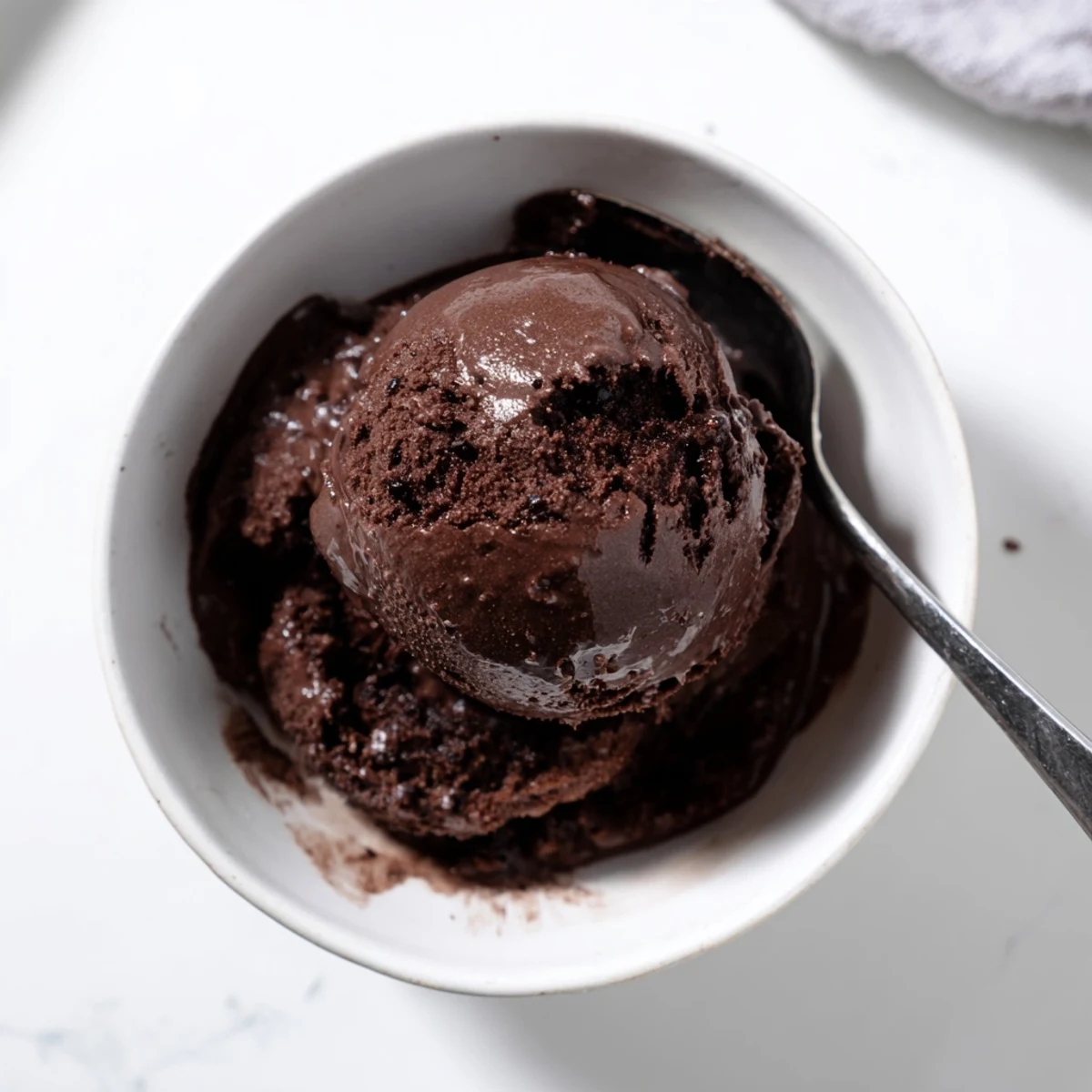 Rich chocolate sourdough ice cream swirling in a glass serving bowl with a silver spoon