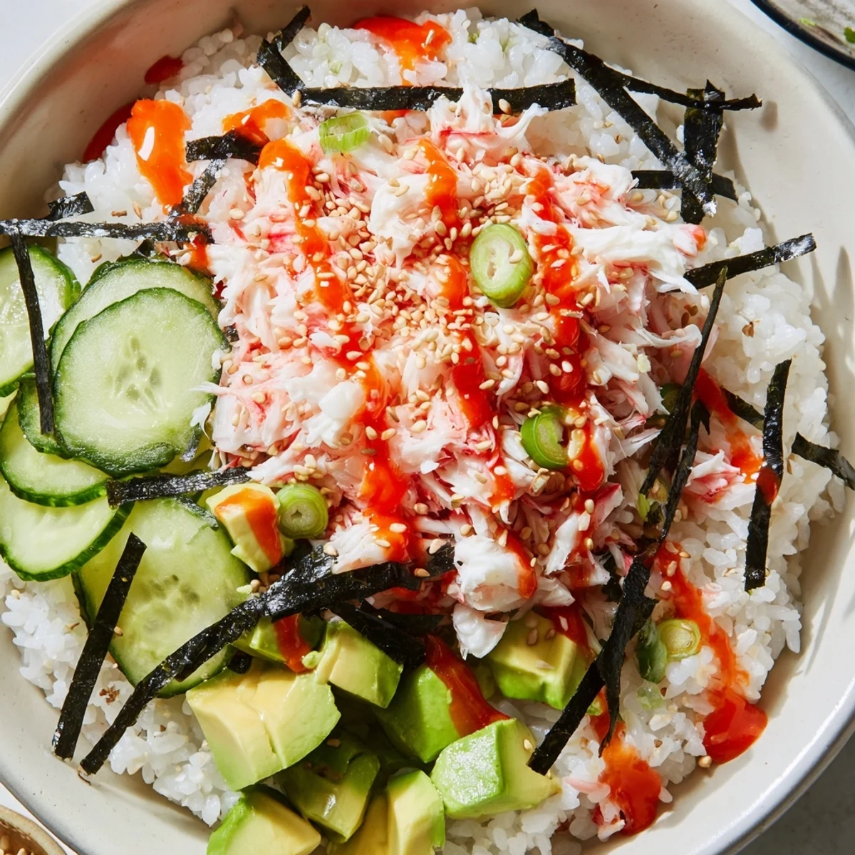 Colorful California roll sushi bowls featuring fluffy rice topped with imitation crab, creamy avocado, and crisp cucumber strips.