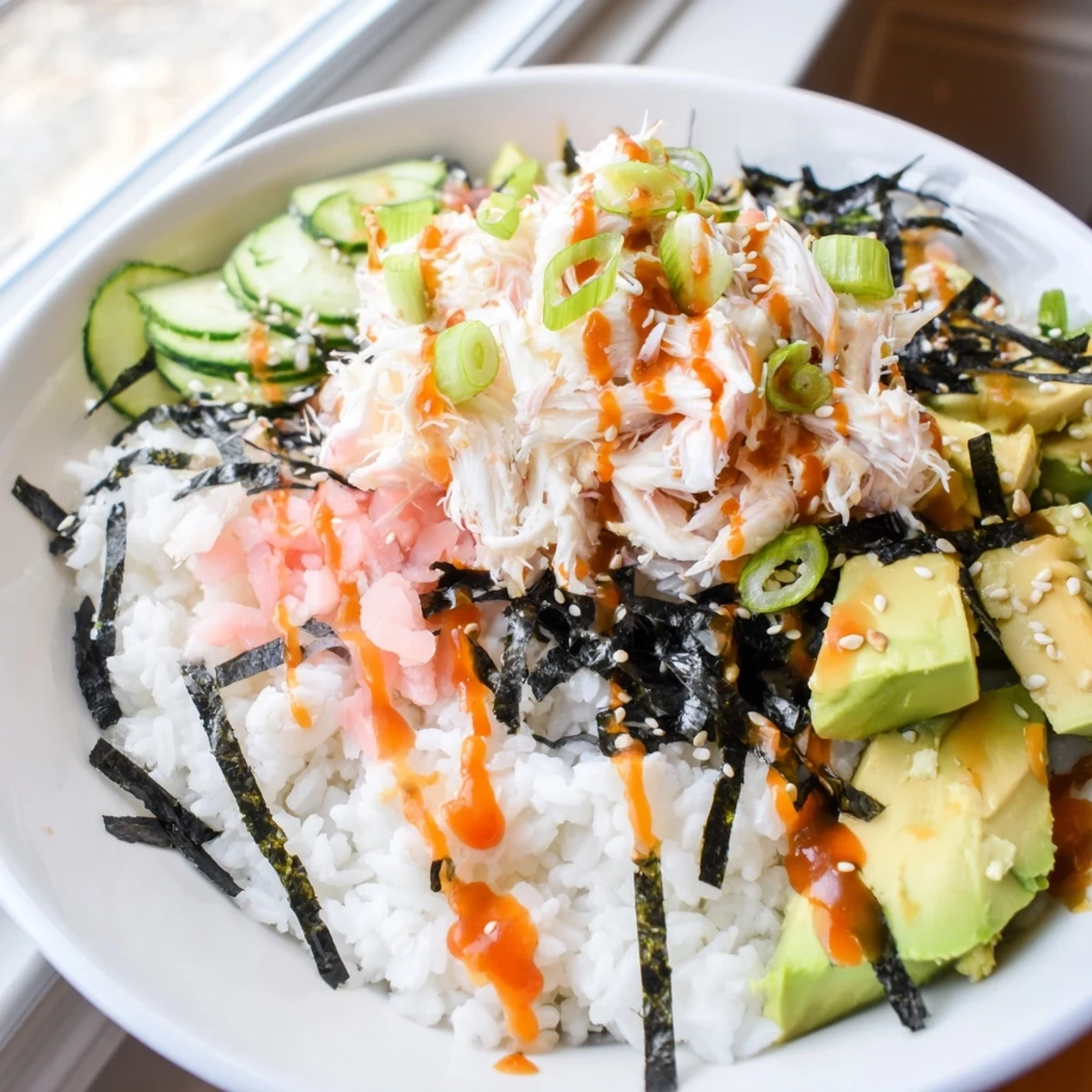 Deconstructed California roll sushi bowl arranged with seasoned rice, shredded crab, fresh avocado, and drizzled spicy mayo.