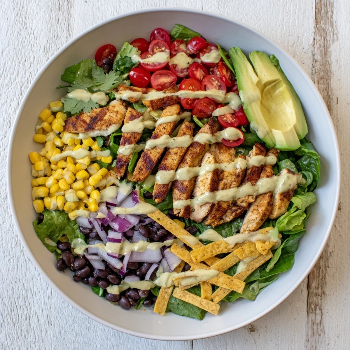 Colorful Southwestern chicken salad with grilled spiced chicken over mixed greens, black beans, avocado, and crisp vegetables drizzled with creamy lime dressing.