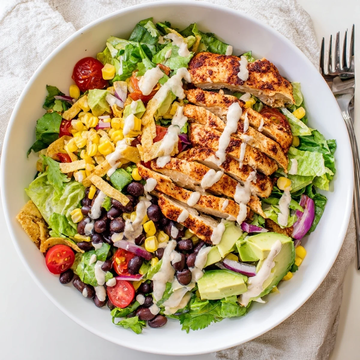 Vibrant bowl of Southwestern chicken salad featuring sliced seasoned chicken breast, fresh corn, cherry tomatoes, and creamy avocado topped with tortilla strips.