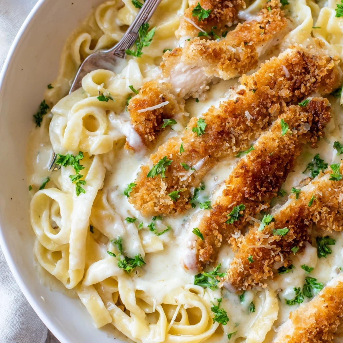 Creamy crispy chicken Alfredo served in a white bowl with parsley garnish and steaming fettuccine