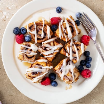 A stack of warm Cinnamon Roll French Toast Bites coated in maple syrup and powdered sugar for a sweet brunch treat.