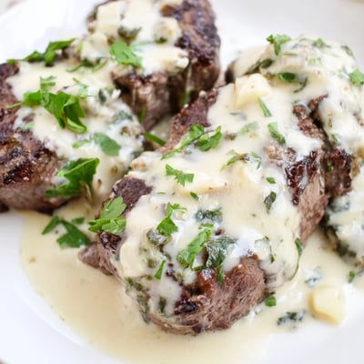 A skillet holds Garlic Butter Steak With Parmesan Cream Sauce beside roasted asparagus for dinner.