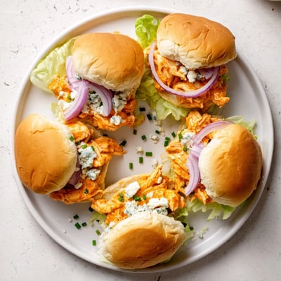 Freshly baked Spicy Buffalo Chicken Sliders arranged on a rustic wooden board, featuring melted blue cheese, crisp lettuce, and vibrant red onion slices for a game day snack.