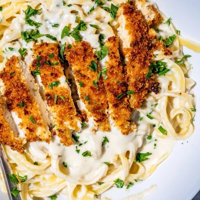 Golden crispy chicken strips nestled atop rich creamy Alfredo pasta on a rustic dinner plate